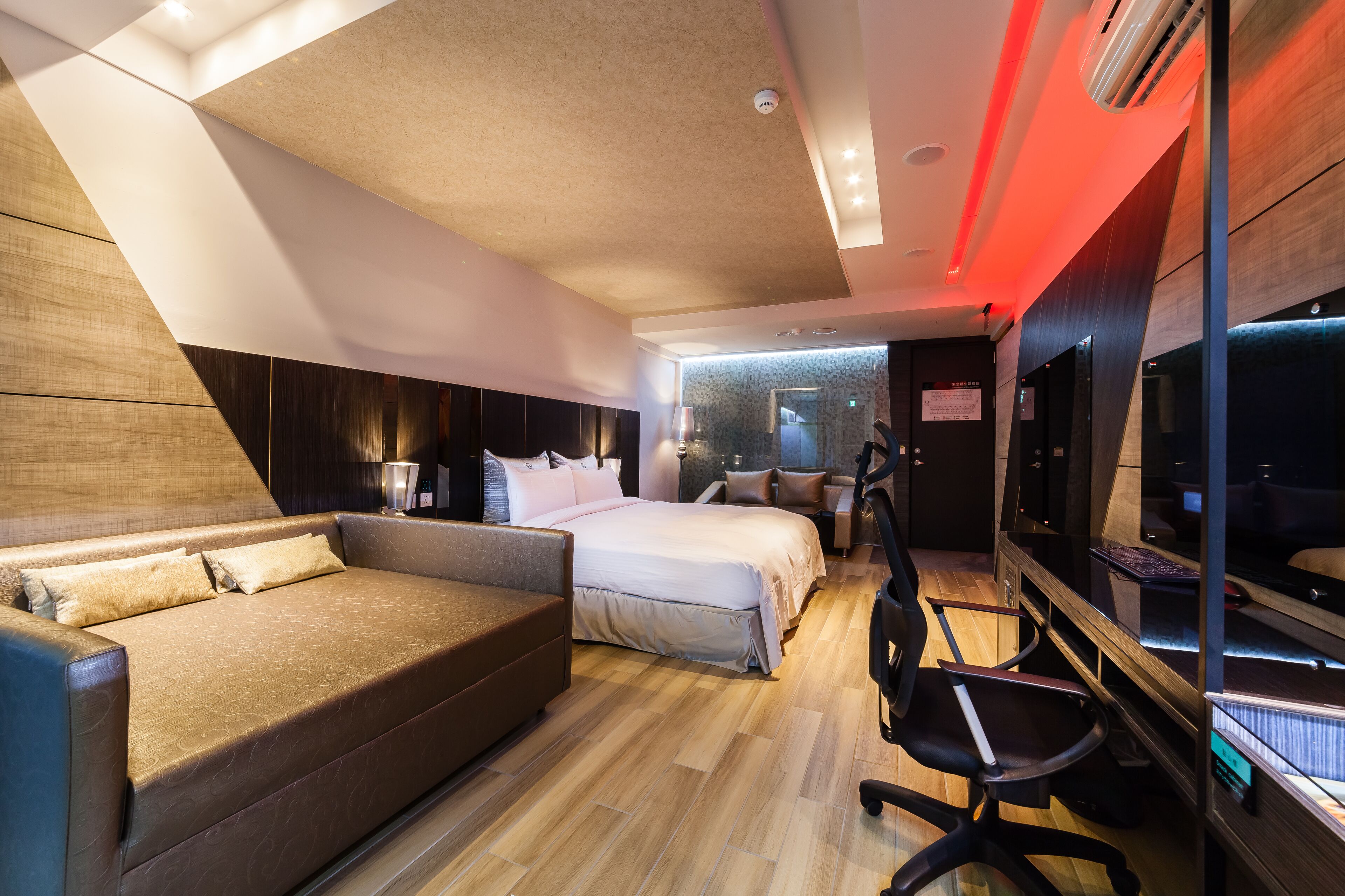 A modern hotel room with a sofa, a bed, a desk, and a TV.
