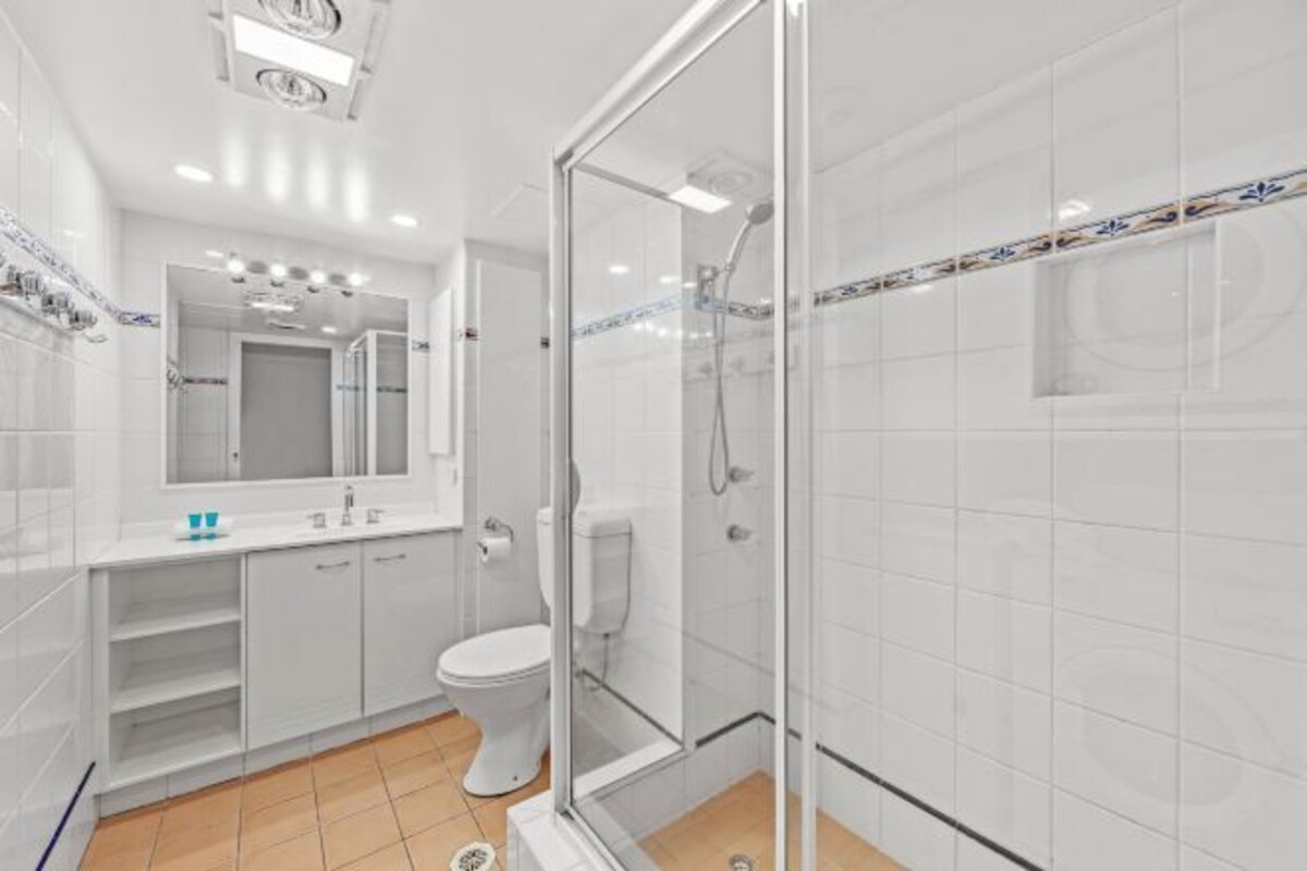 Une salle de bain moderne avec une douche à parois de verre, des toilettes blanches et un meuble-lavabo avec un miroir.