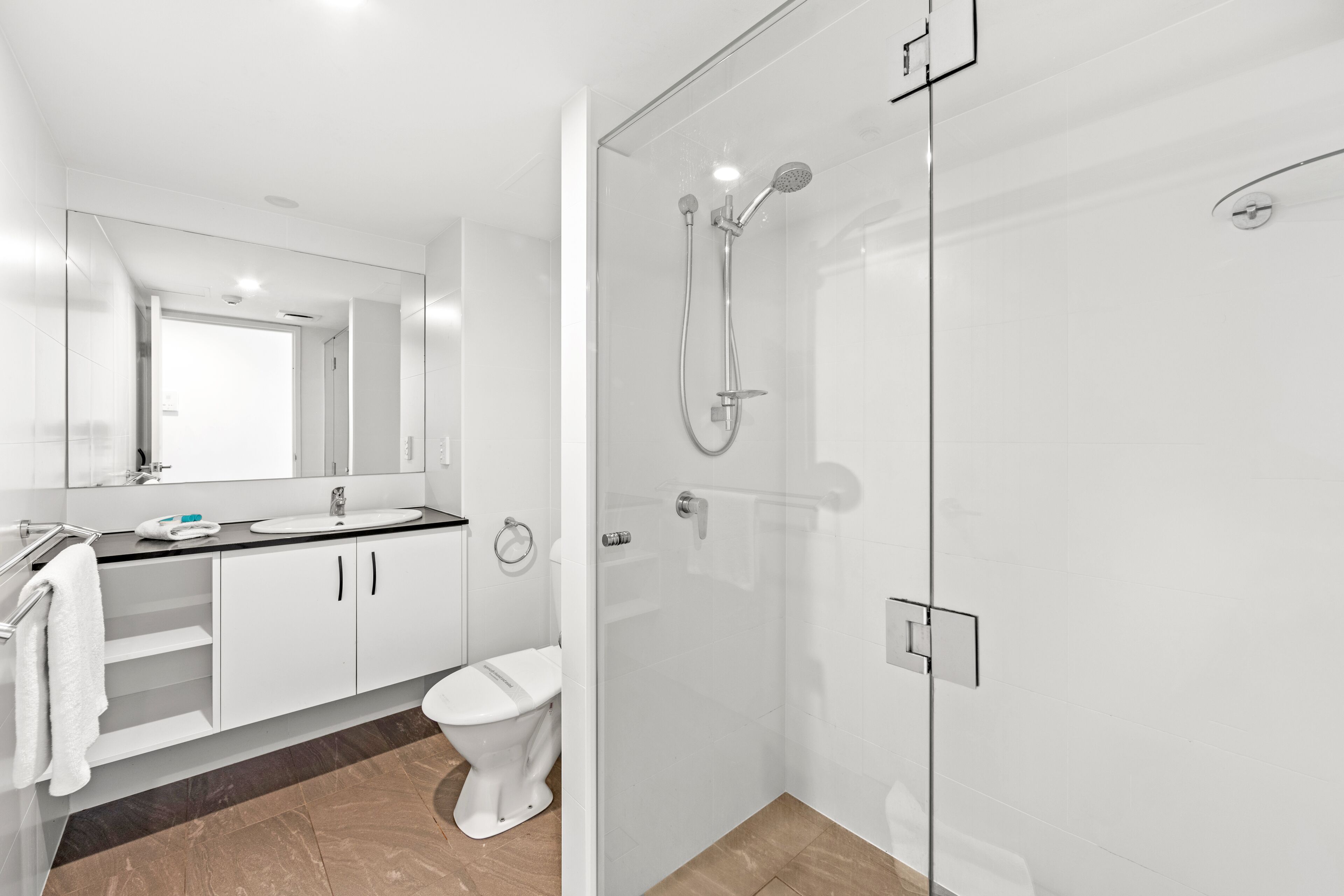A modern bathroom with a glass-enclosed shower, a white toilet, and a vanity with a mirror.