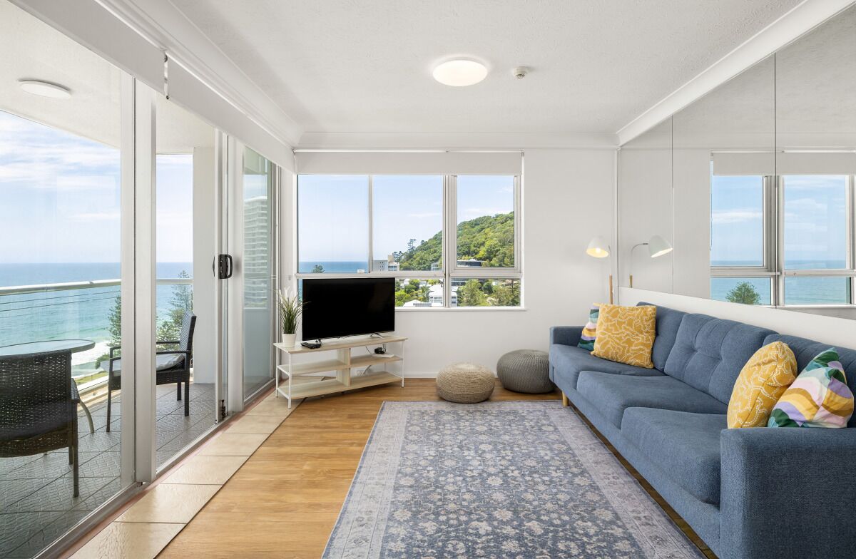 A modern living room with a TV, sofa, and large windows overlooking the sea.