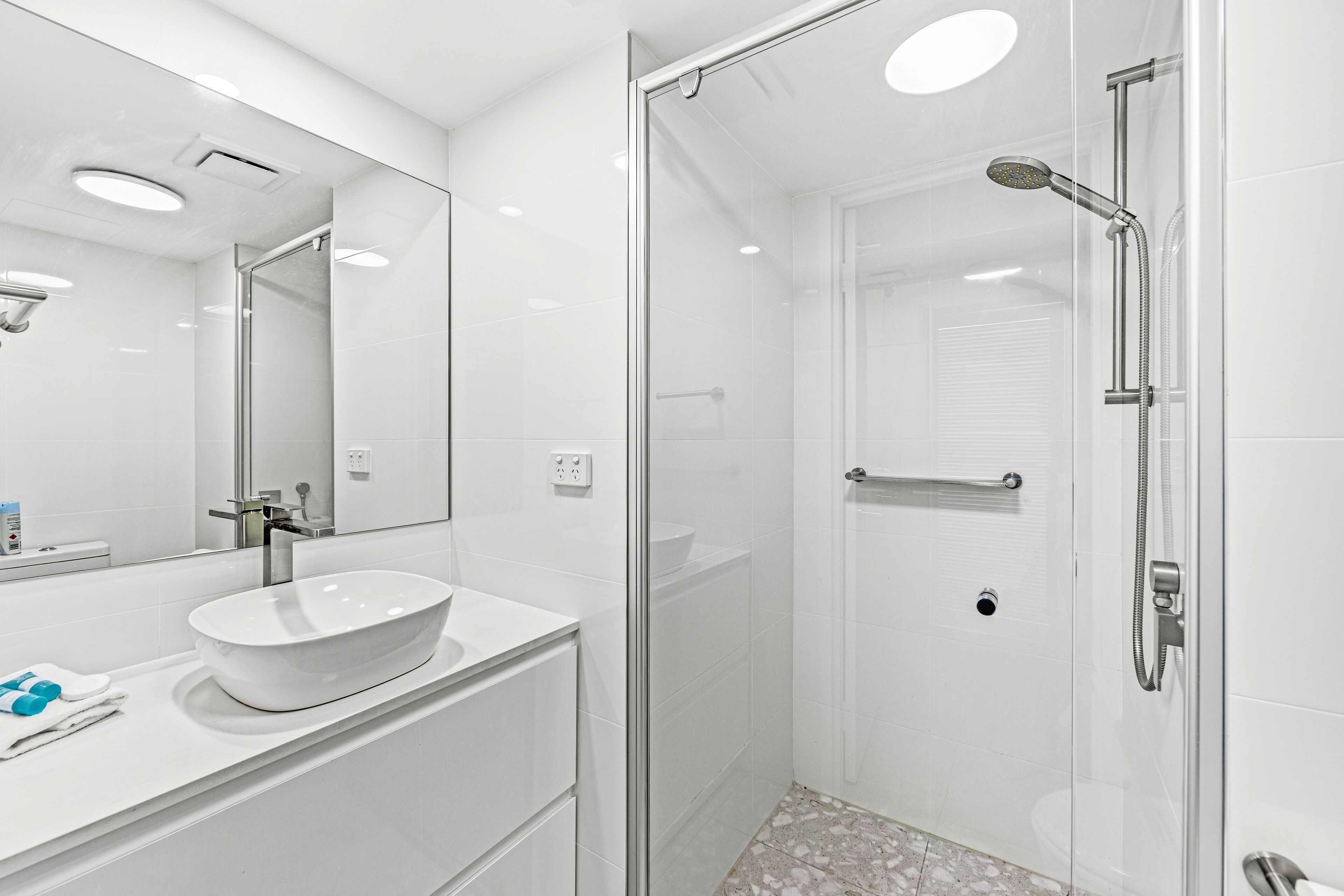 Une salle de bain moderne avec une douche à parois de verre, un lavabo blanc et un grand miroir.
