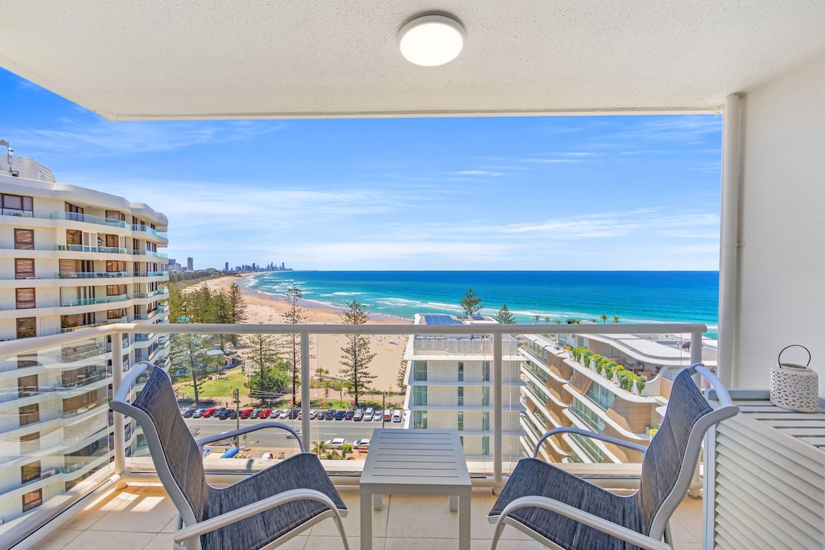 A balcony with a view of the beach and ocean, furnished with chairs and a table.