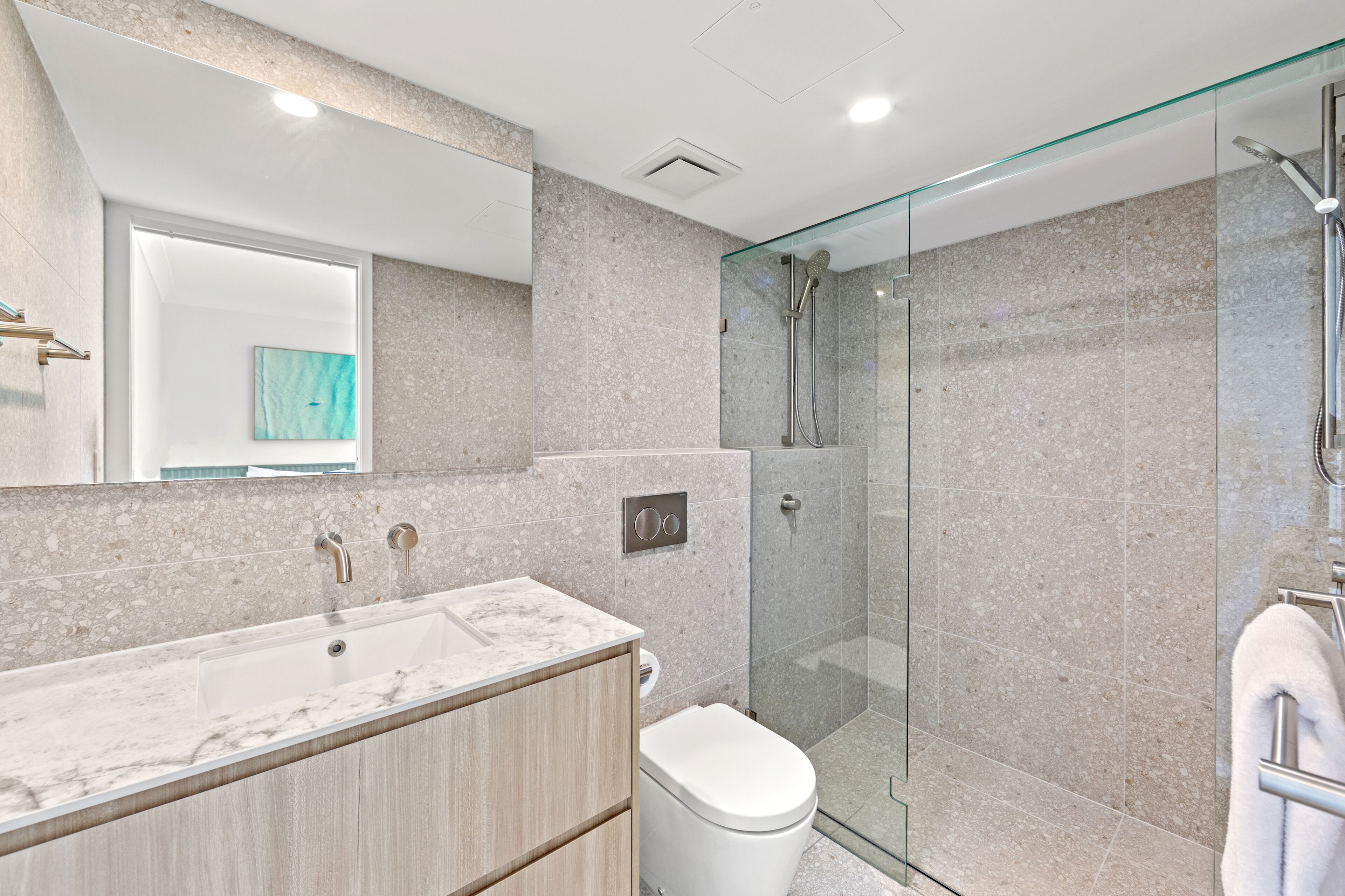 Ein modernes Badezimmer mit Marmorwaschbecken, einer Duschkabine aus Glas und einer Toilette.