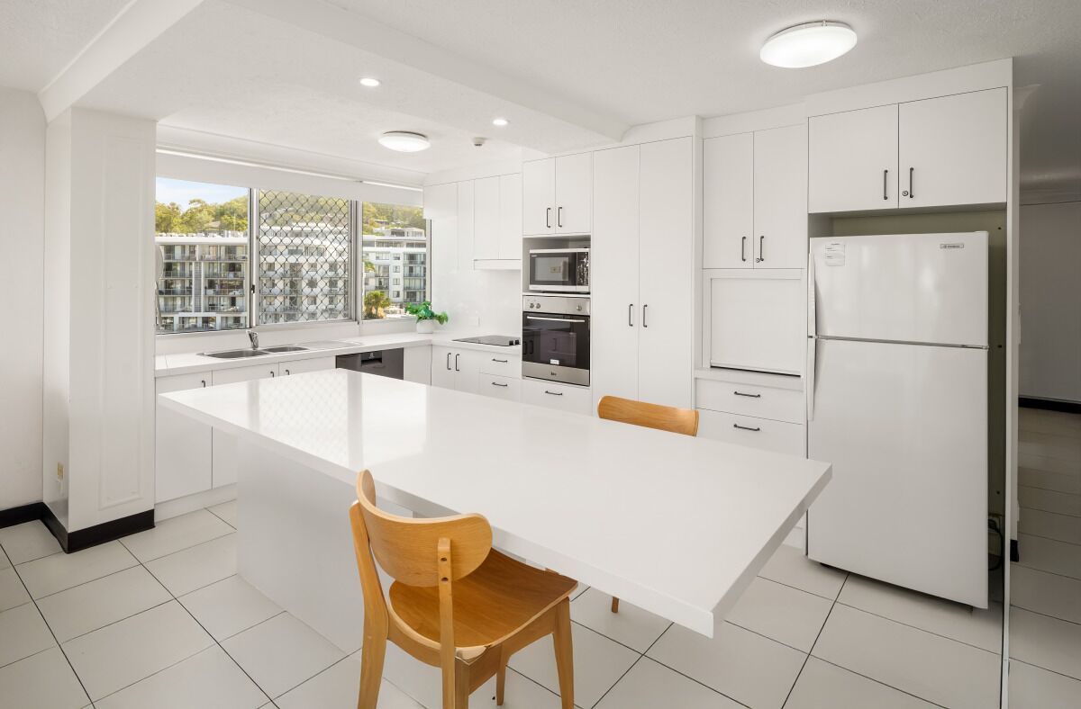 A modern kitchen with white cabinetry, a central island, and a view of a residential area.