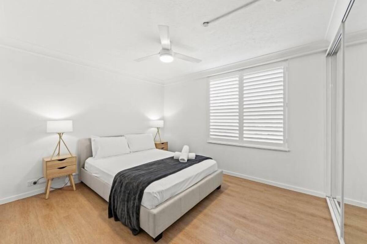 A bedroom with a bed, bedside tables, a ceiling fan, and a window with blinds.