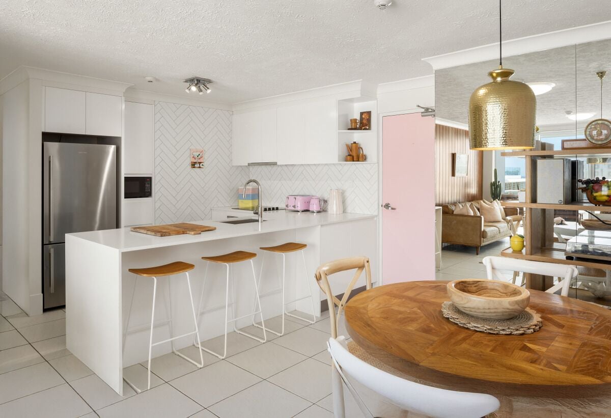 A modern kitchen with a central island, bar stools, a wooden dining table, and a pendant light.