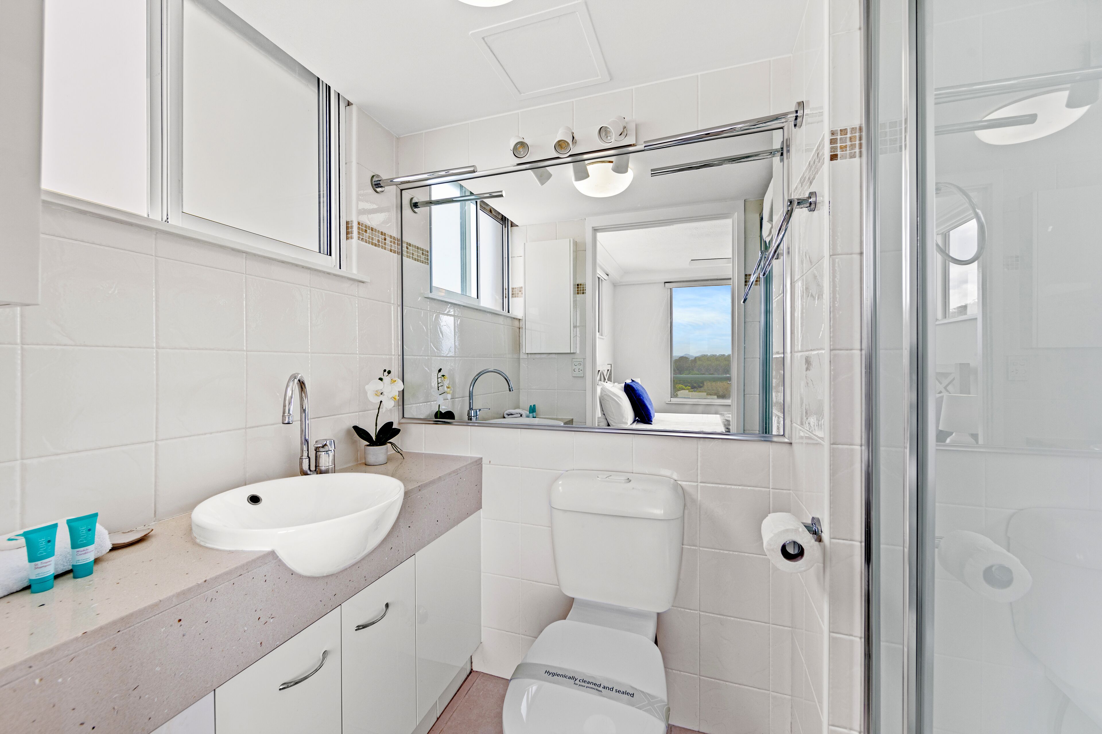 Un baño moderno con lavamanos, inodoro y zona de ducha blancos.