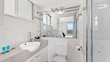 Un baño moderno con lavamanos, inodoro y zona de ducha blancos.