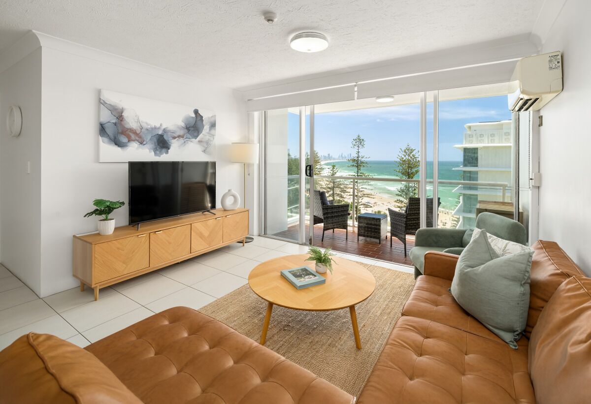 A modern living room with a sofa, coffee table, TV, and a balcony with a view of the ocean.