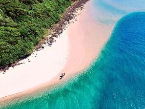 Vista aérea de una playa con aguas turquesas cristalinas, una orilla arenosa y vegetación verde exuberante a lo largo de la costa.