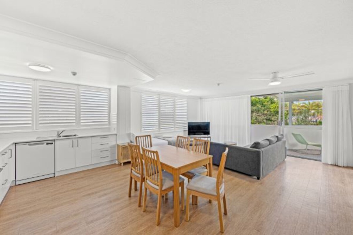 Une cuisine moderne avec des meubles blancs, une table à manger avec des chaises, un canapé gris et un balcon avec vue.