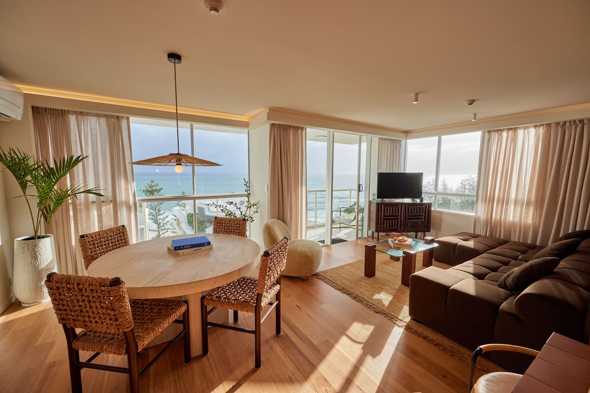 A spacious living room with a large sofa, a dining table with chairs, and a TV stand.