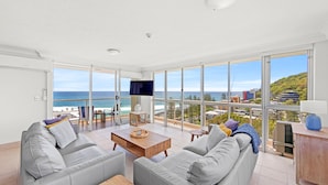 A spacious living room with a large window overlooking the beach and cityscape. - Burleigh Beach Tower (Burleigh Heads)