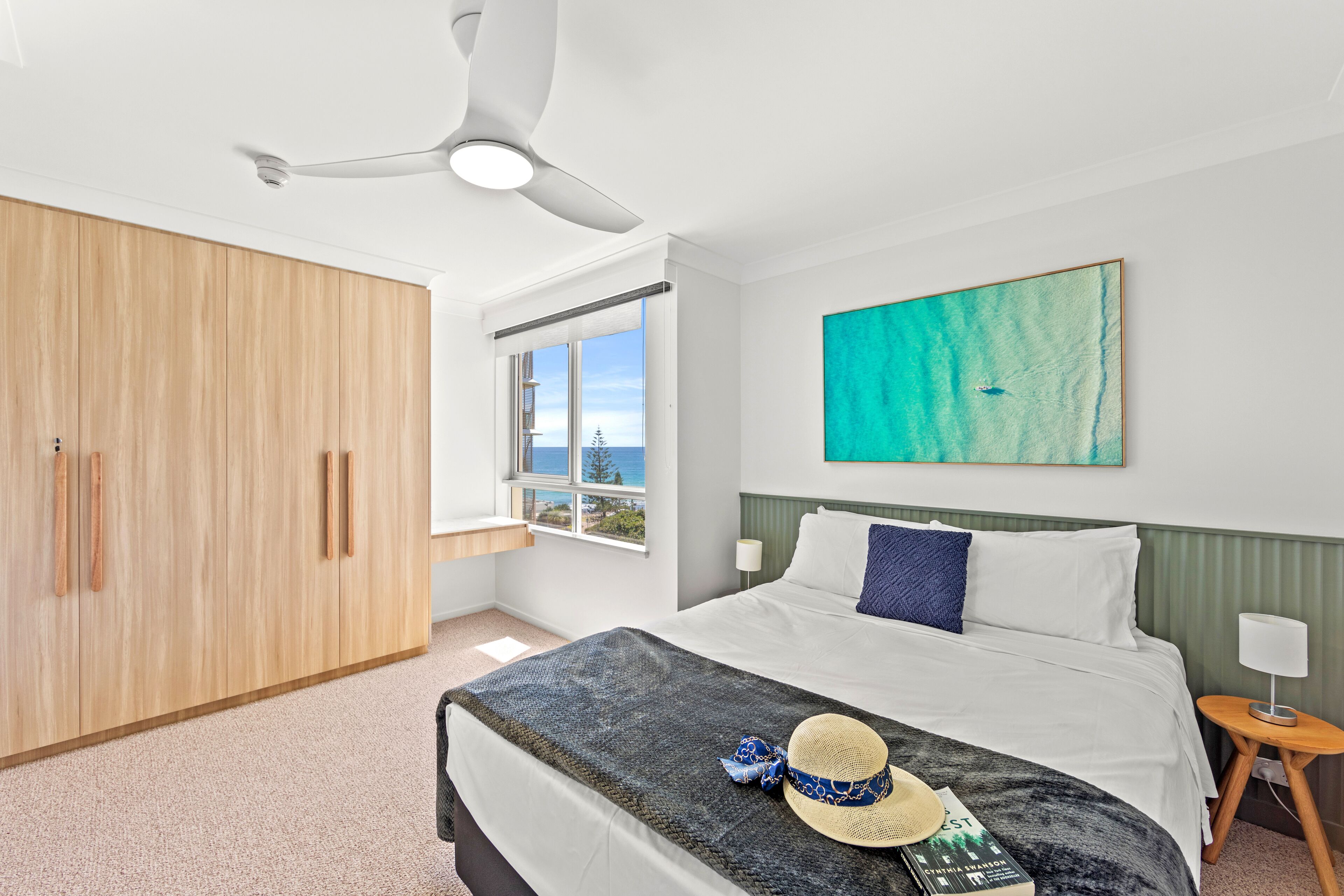 Ein Schlafzimmer mit Bett, Deckenventilator, Fenster mit Aussicht, Kleiderschrank und einem Gemälde an der Wand.