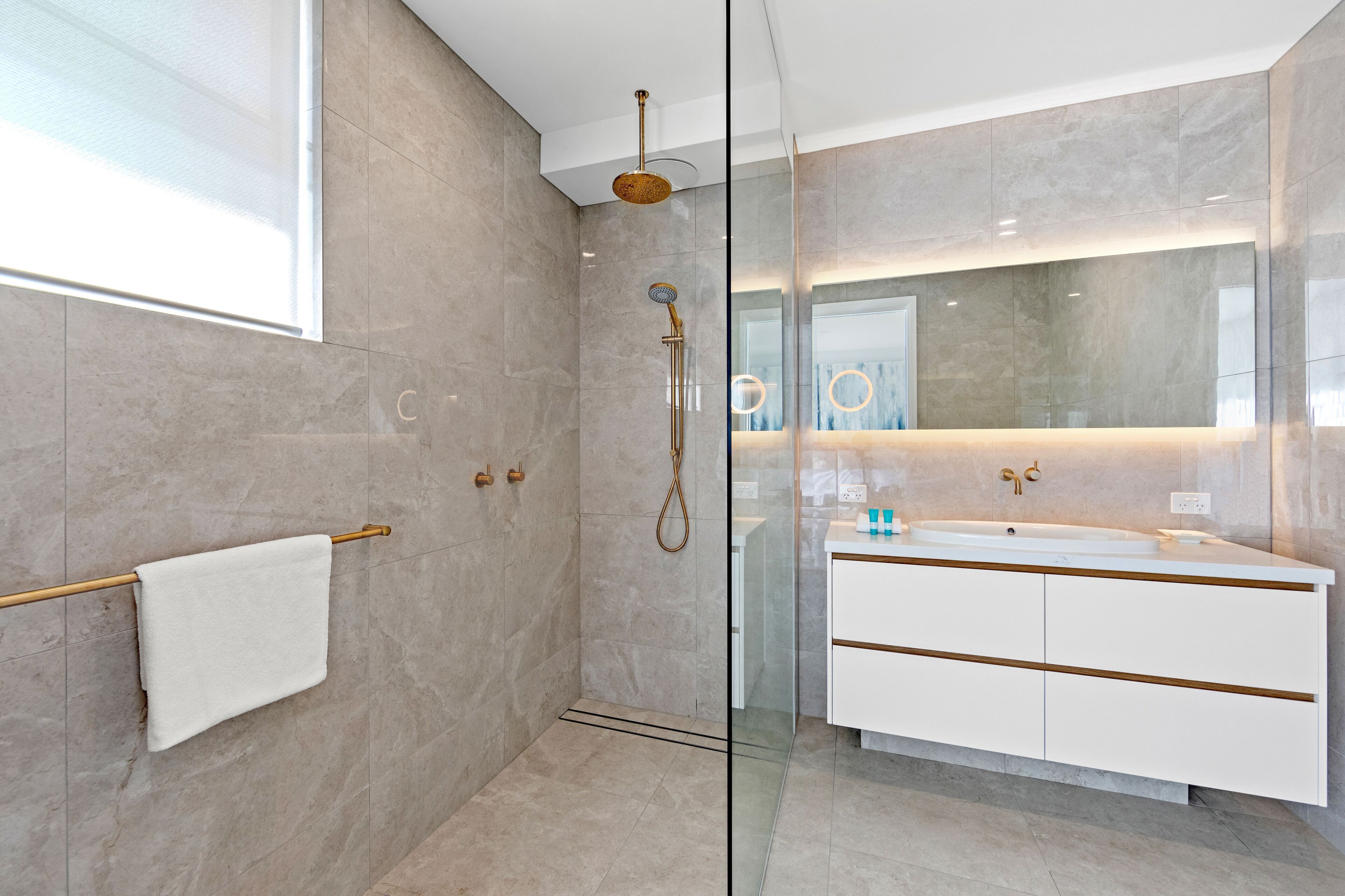 A modern bathroom with a glass-enclosed shower, a white vanity with gold accents, and a large mirror.