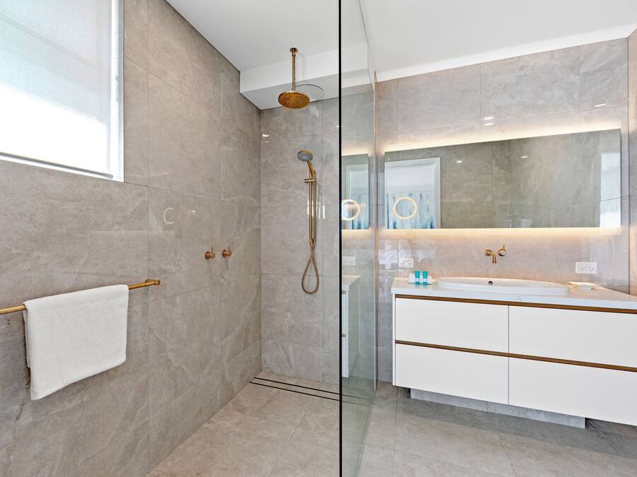 A modern bathroom with a glass-enclosed shower, a white vanity with gold accents, and a large mirror.