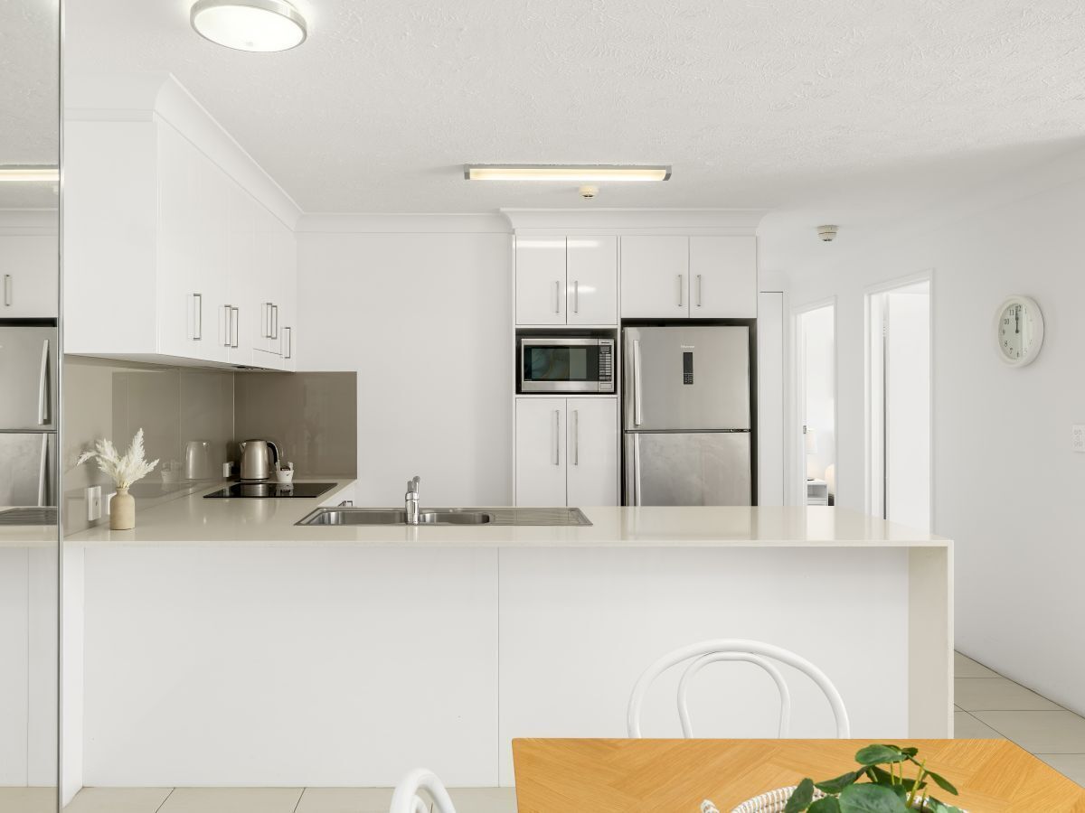 A modern kitchen with white cabinetry, stainless steel appliances, and a wooden dining table.