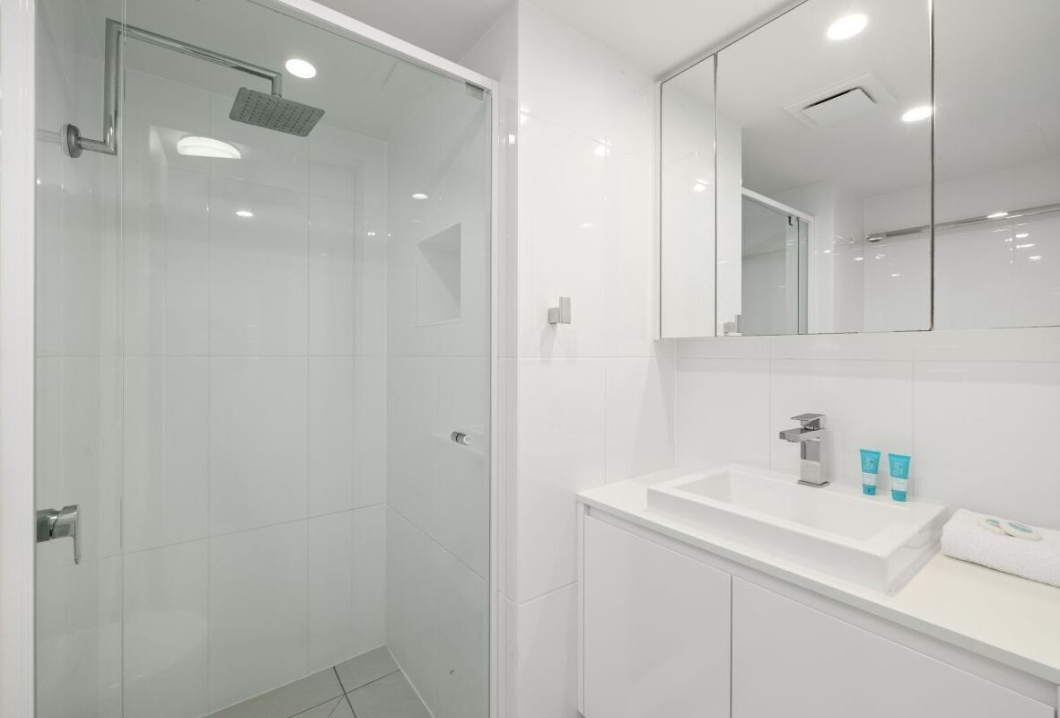 Ein modernes Badezimmer mit einer Duschkabine aus Glas, einem weißen Waschbecken und einem Spiegel über der Waschtischablage.