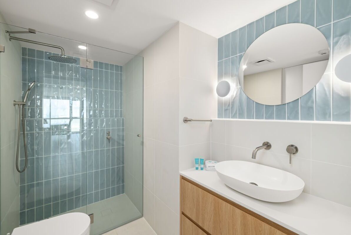 Un baño moderno con cabina de ducha de vidrio, un lavabo blanco y un espejo grande.