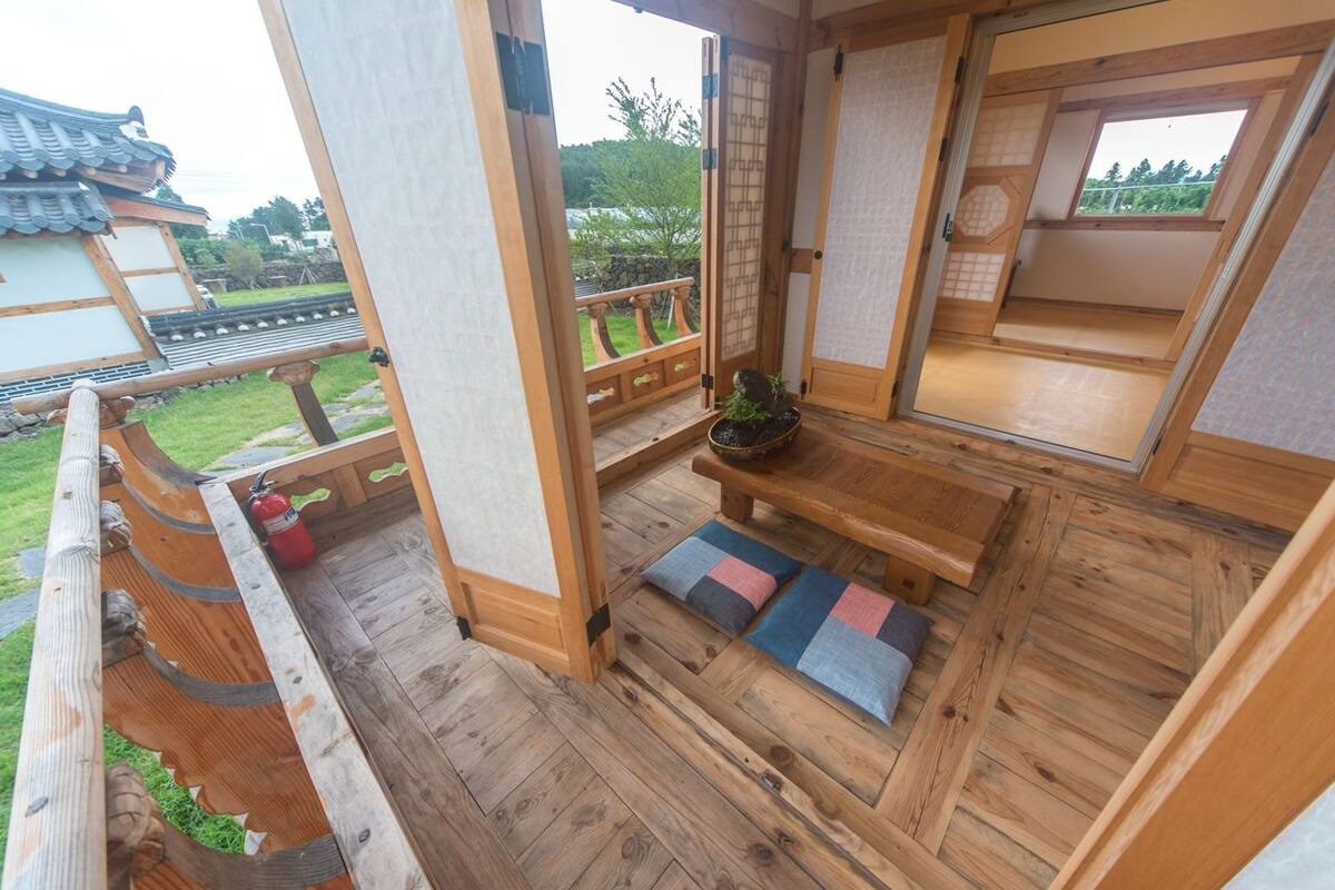 Una habitación tradicional japonesa con suelo de tatami, un banco de madera bajo y vista a un jardín.