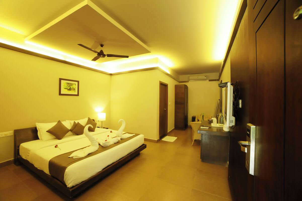 A hotel room with a bed, a desk, a chair, a ceiling fan, and a door.