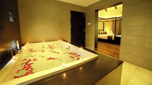 A modern spa room with a large bathtub filled with water and rose petals, surrounded by candles. - Broad Bean Resort & Spa (Devikolam)