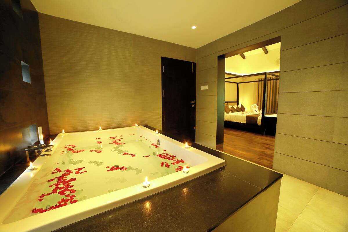 A modern spa room with a large bathtub filled with water and rose petals, surrounded by candles.