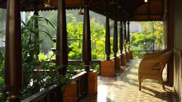 A covered outdoor area with wooden pillars, a wicker chair, and potted plants. - Broad Bean Resort & Spa (Devikolam)