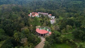 An aerial view of a resort with multiple buildings, a central circular structure, and surrounding lush greenery. - Broad Bean Resort & Spa (Devikolam)