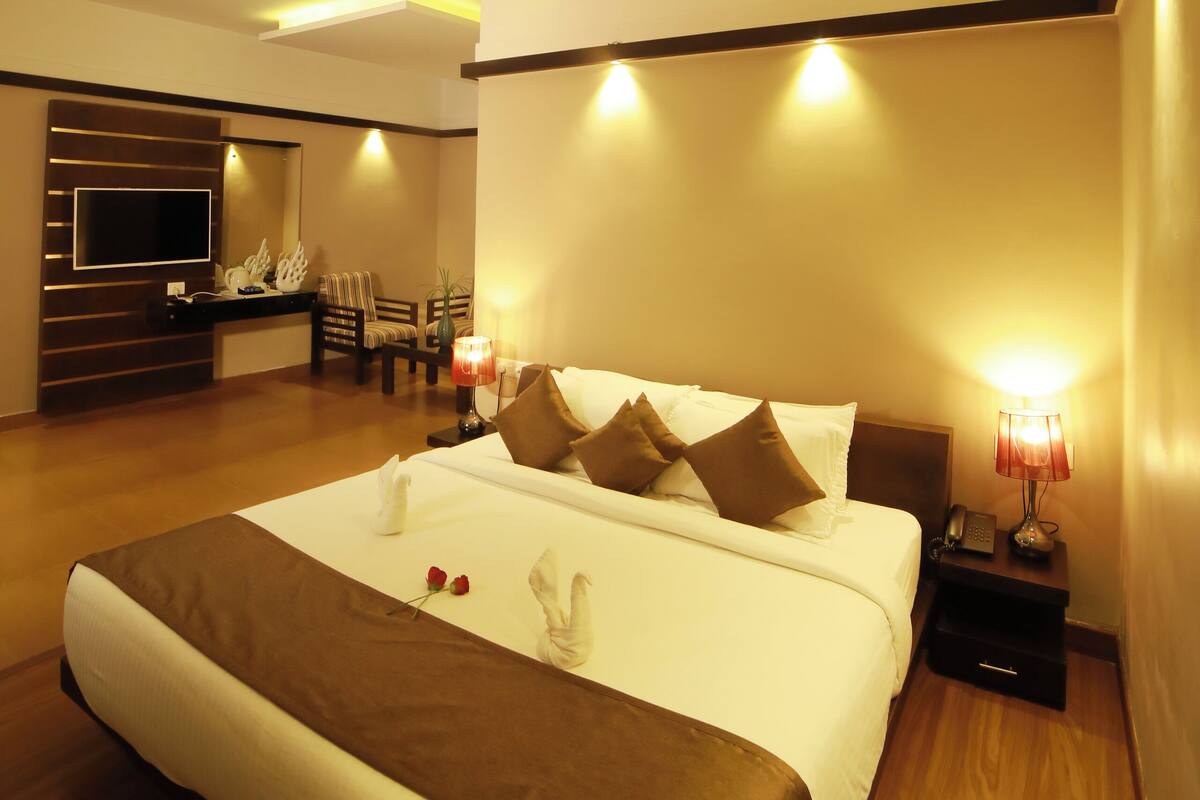A hotel room with a large bed, a ceiling fan, a flat-screen TV, and a seating area with a table and chairs.