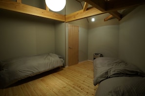 Une petite pièce à la lumière tamisée, avec deux lits simples, des poutres en bois au plafond et une porte.