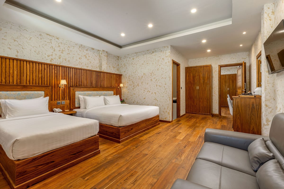 A hotel room with two beds, a sofa, wooden paneling, a TV, and a wooden dresser.