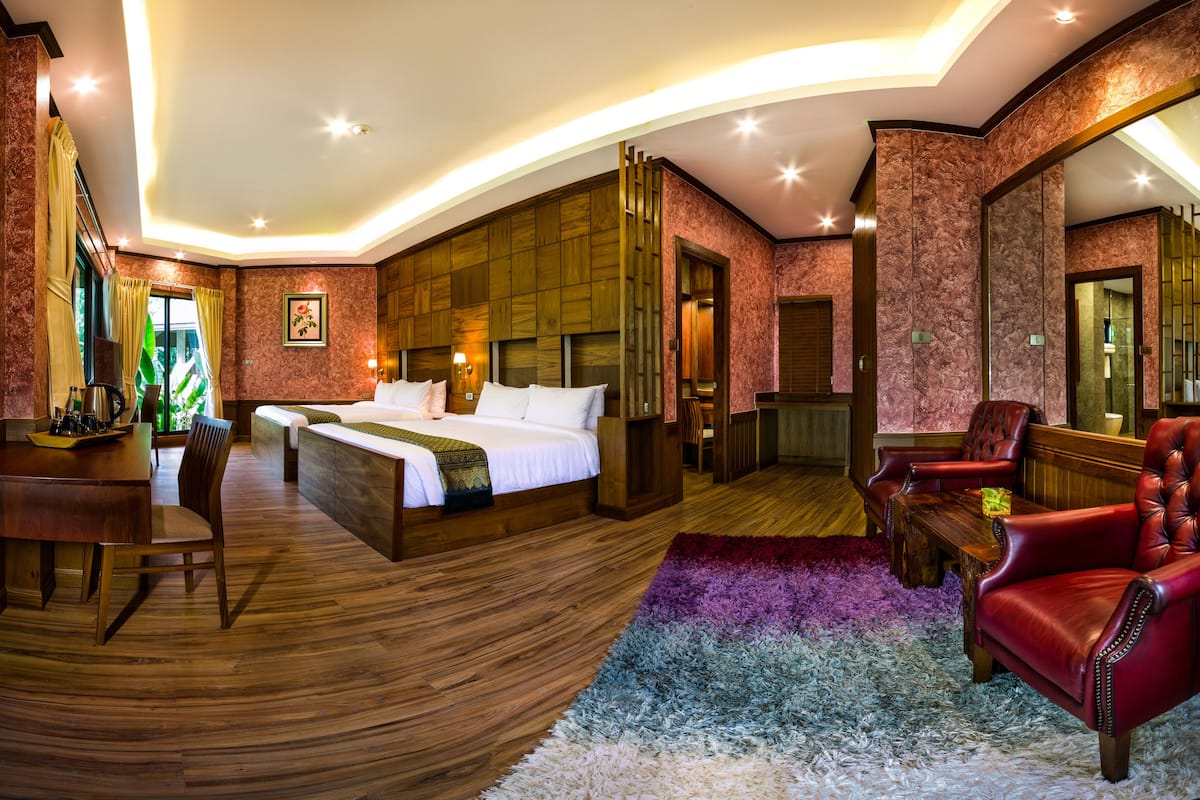 A spacious hotel room with a large bed, a desk, a leather armchair, and a bathroom visible through an open door.