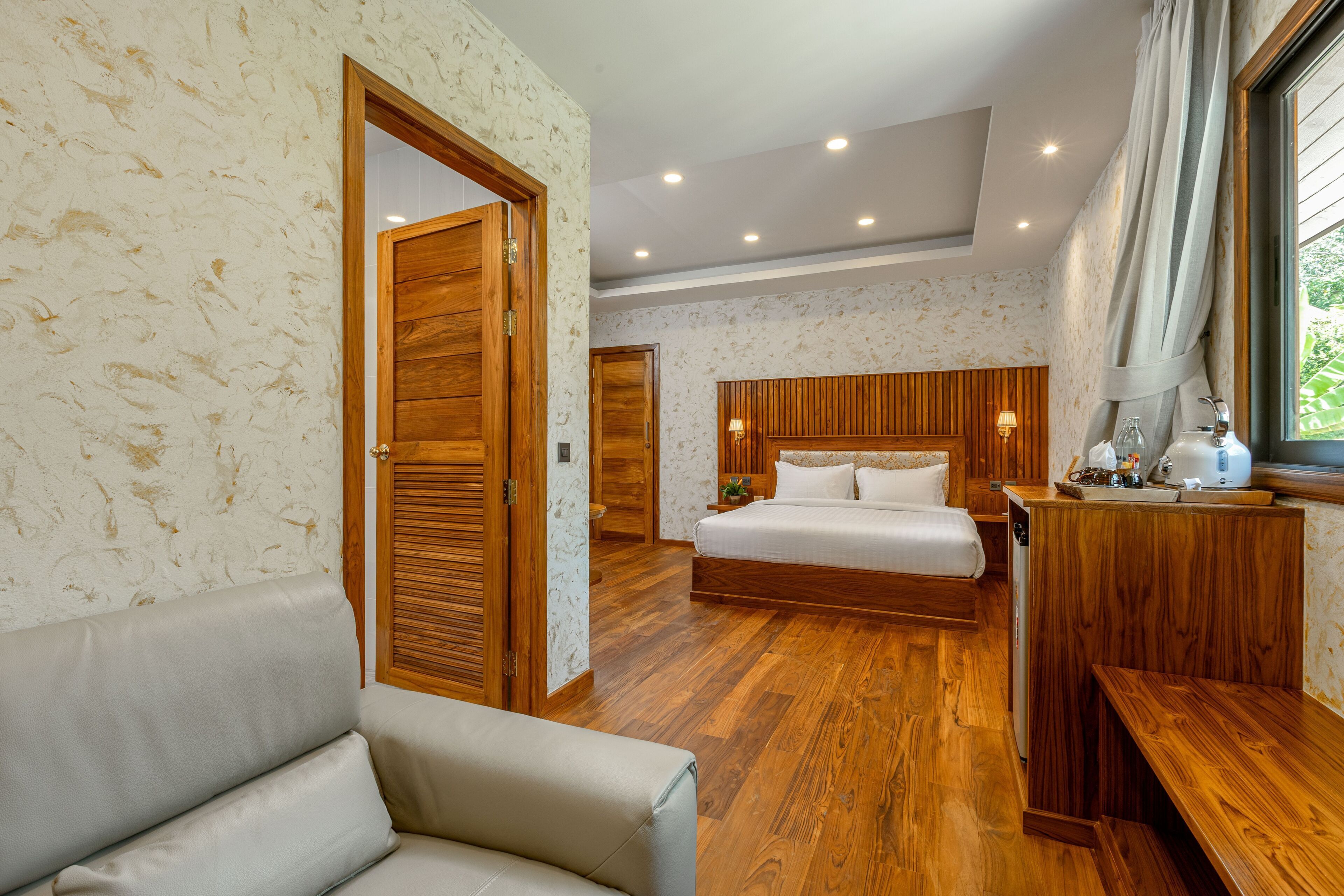 Une chambre à coucher avec un lit en bois, un bureau en bois, un canapé et une porte donnant sur une autre pièce.