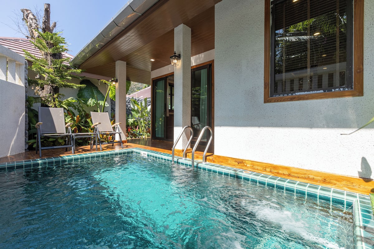 A swimming pool with a wooden deck, a covered seating area, and a view of a building with large windows.