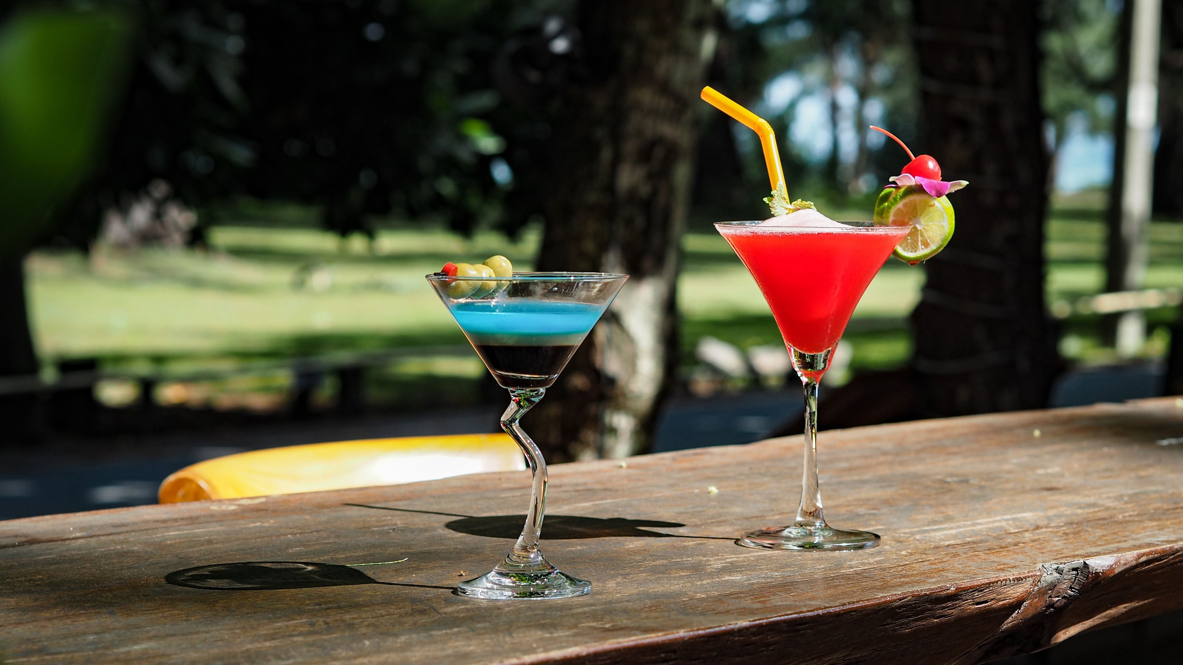 Deux cocktails sur une table en bois, à l’extérieur, avec un arrière-plan flou composé d’arbres et d’un terrain de golf.