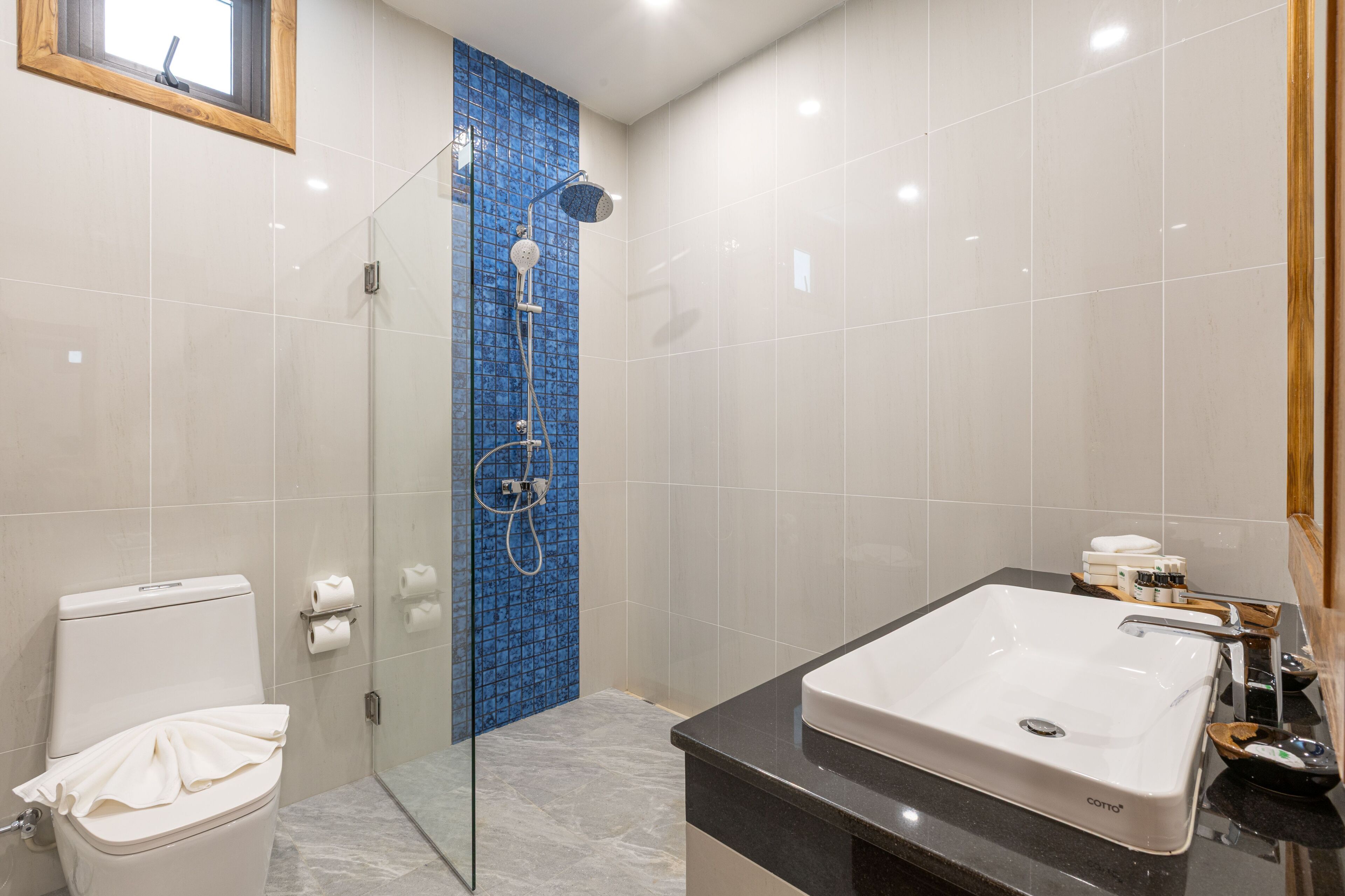 A bathroom with a glass shower enclosure, a white sink with a black countertop, and a toilet with a towel on it.