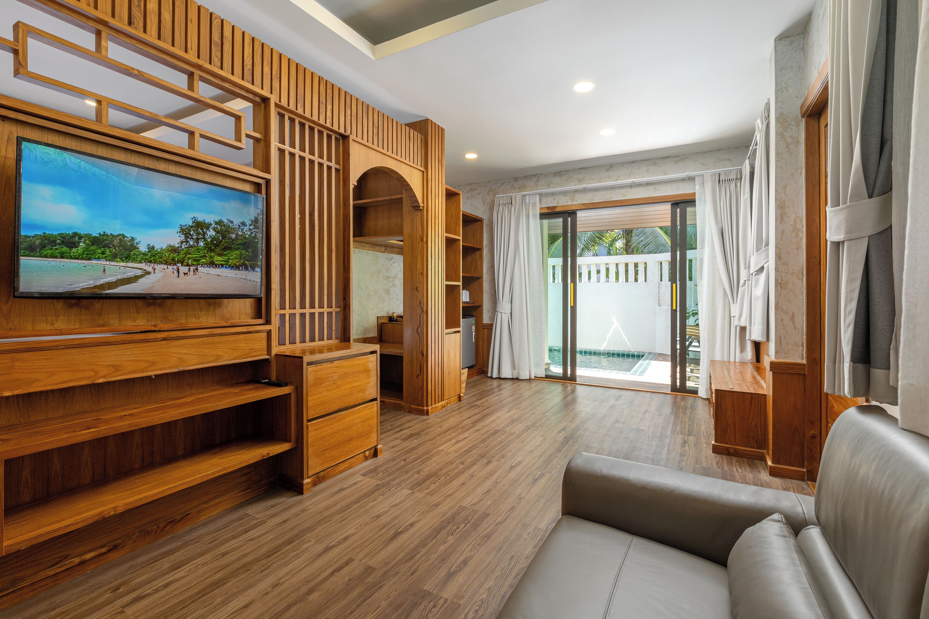 A modern living room with a large flat-screen TV, wooden shelving, a sofa, and a sliding glass door leading to an outdoor area.