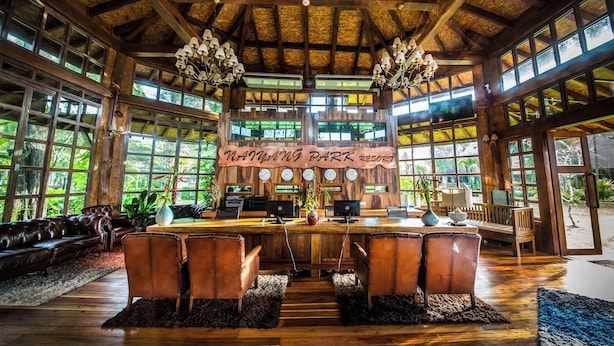 Un vestíbulo espacioso con un mostrador de recepción de madera, asientos de cuero y grandes ventanales con vistas al exterior.