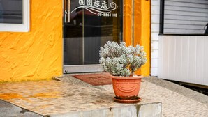 A potted plant in front of a building with a glass door and a sign with Chinese characters. - Wei Yuan Hotel (Hengchun)