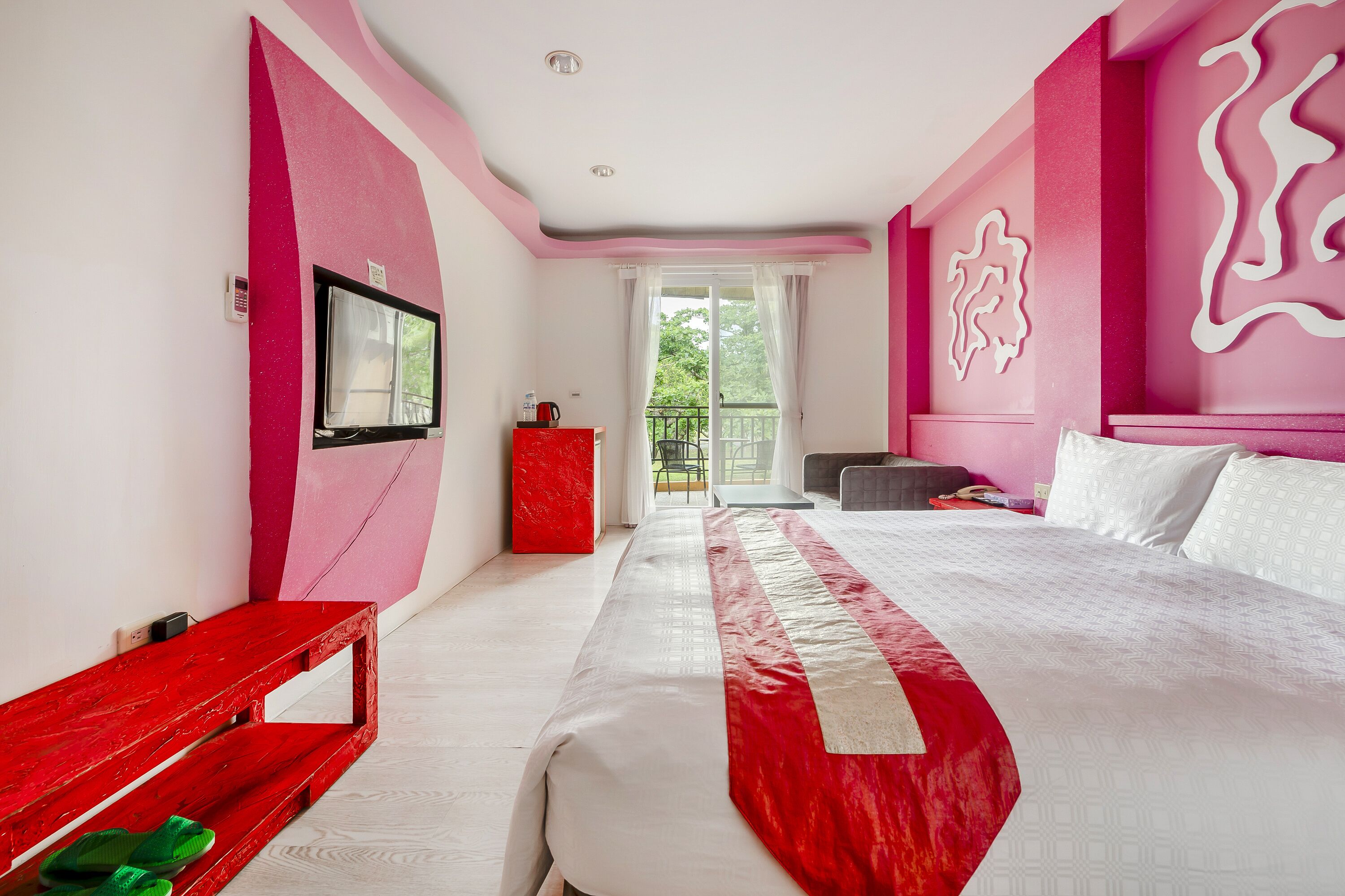 A bedroom with a large bed, a red bench, a window, and a balcony.
