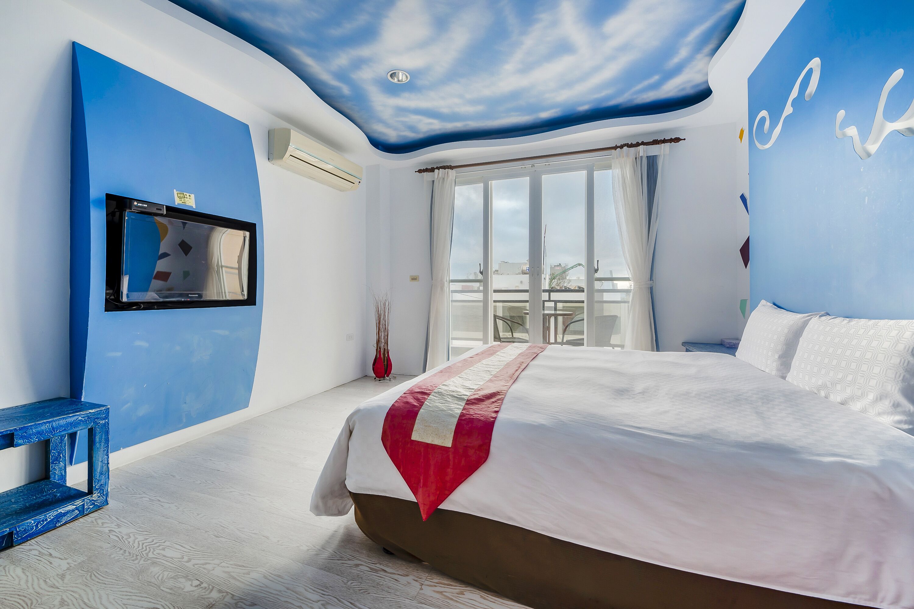 A bedroom with a large bed, a ceiling with a cloud design, a window with curtains, and a blue wall.