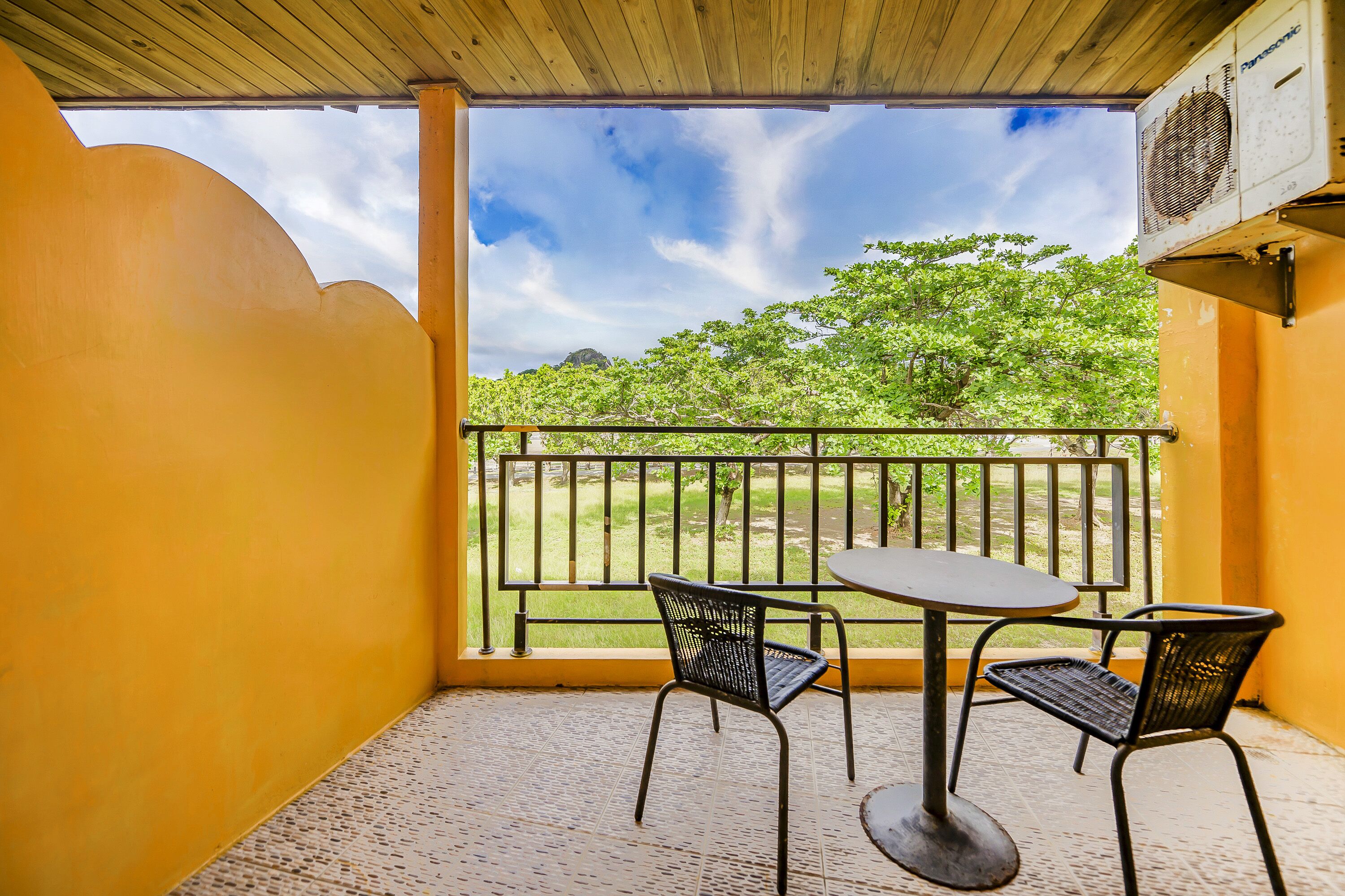 A balcony with a table and two chairs, overlooking a green landscape and a clear sky.