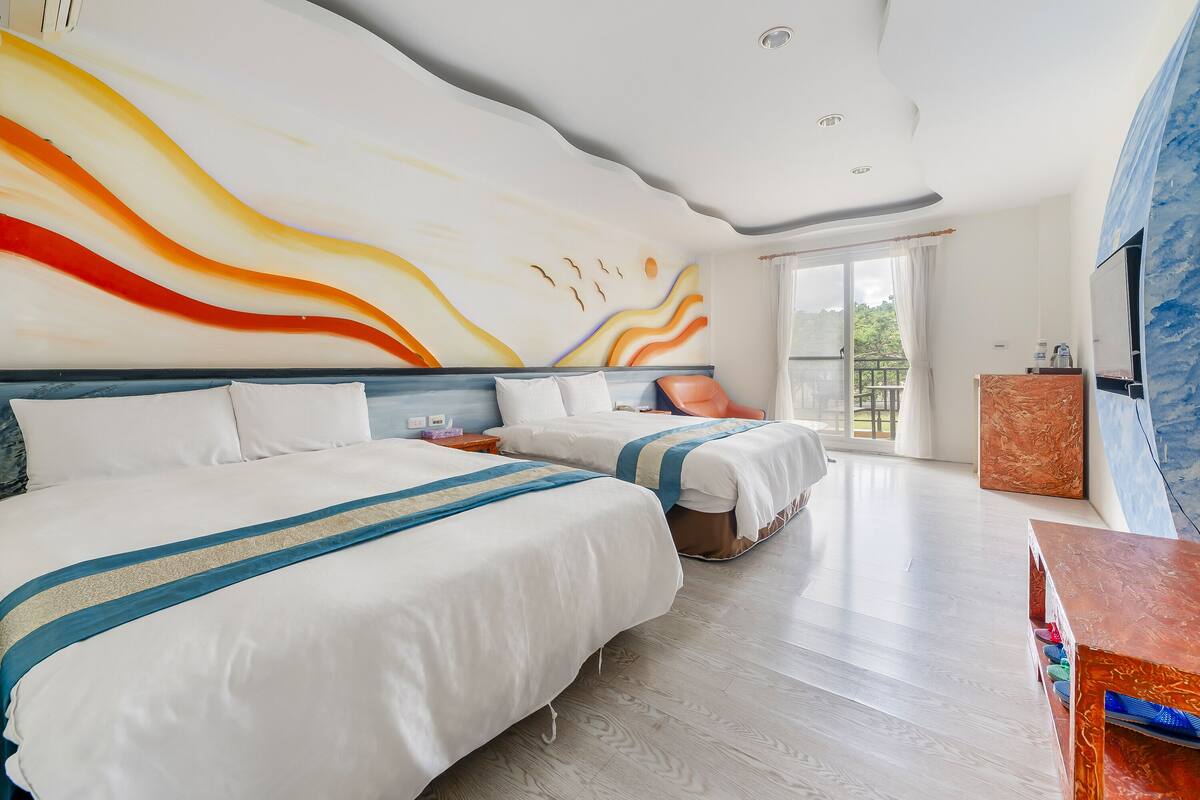 A hotel room with two beds, a large abstract mural, a wooden floor, and a balcony with a view.