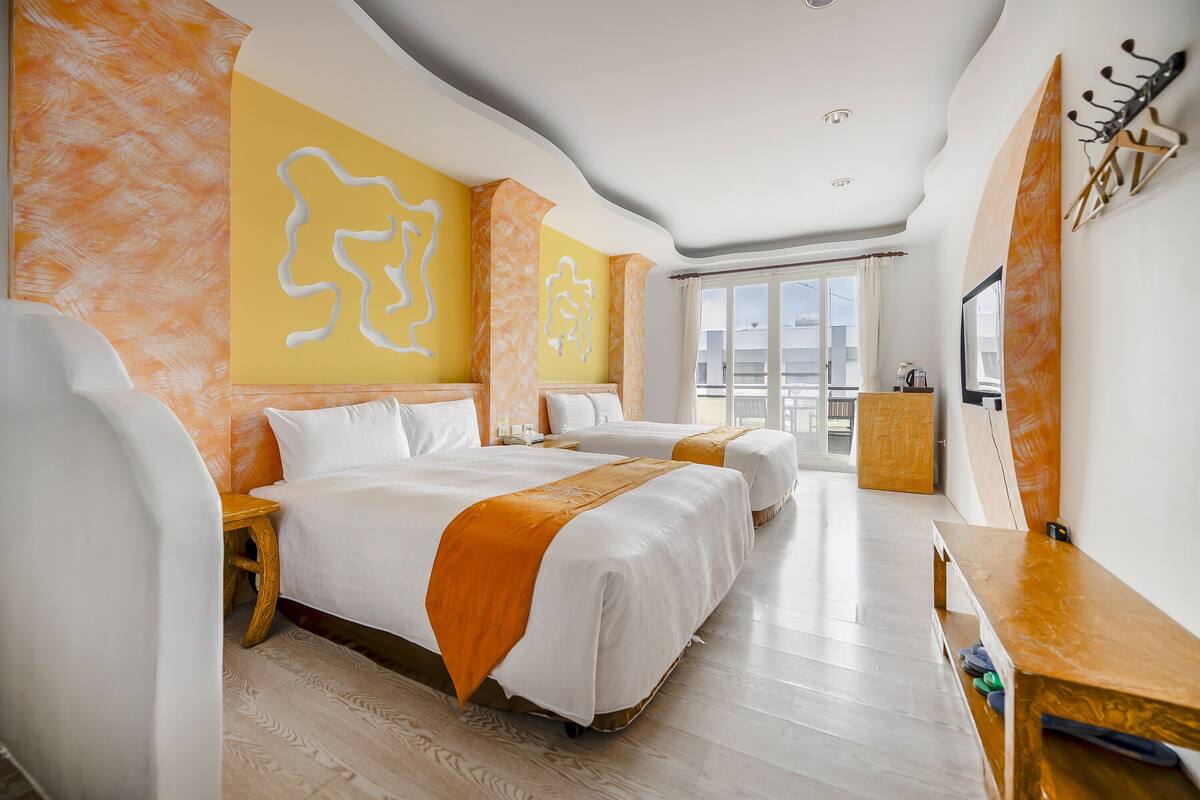 A hotel room with two beds, a wooden bench, a TV, and a large window.