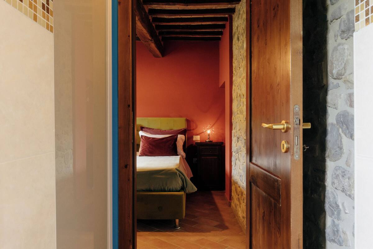 A narrow hallway leading to a bedroom with a bed, a nightstand, and a stone wall.