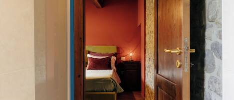 A narrow hallway leading to a bedroom with a bed, a nightstand, and a stone wall.