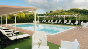 A poolside area with lounge chairs, a pergola, and a view of a landscaped garden. - Casale Serena 1912 (Fabro)