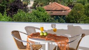 A balcony with wicker chairs, a table with two glasses of orange juice and two apples, and a view of a building with a red-tiled roof. - Studio Stars (Zakynthos)