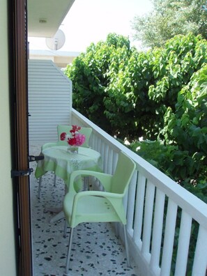 A balcony with two green plastic chairs and a table, each with a vase of flowers. - Studio Stars (Zakynthos)